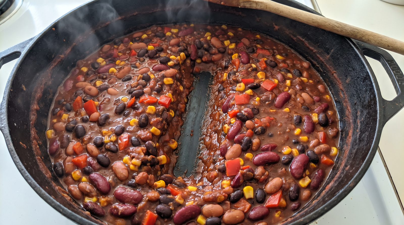 A wooden spoon dragged through a pot of thick three bean chili leaving a channel that holds its shape