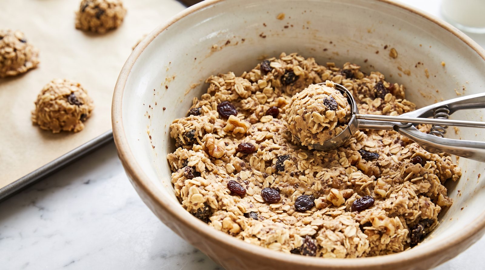 Oatmeal cookie dough with rolled oats, raisins, walnuts and ground flaxseed being scooped onto a baking tray