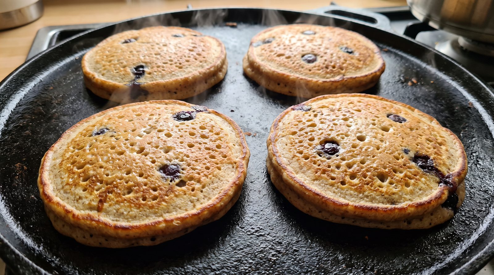 Thick wholegrain pancakes cooking on a cast iron griddle with bubbles breaking on the surface