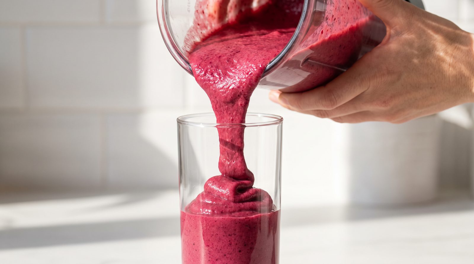 A thick deep pink high fiber smoothie being poured into a tall glass
